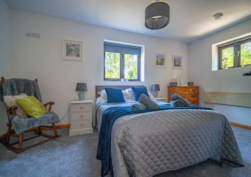 Bright bedroom with double bed, blue bedding, wooden furniture, rocking chair and windows