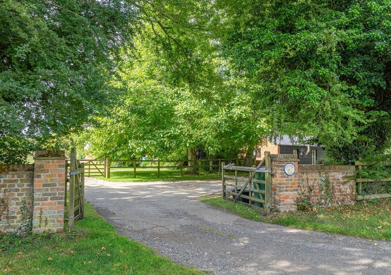 Tree-lined driveway with brick gate pillars and wooden fencing leading to property