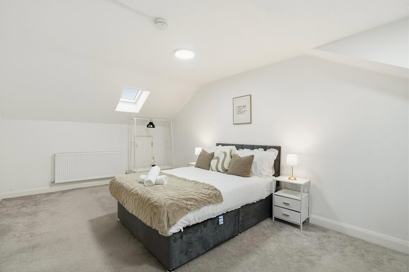 Bright attic bedroom with double bed, white bedside table, skylight window and neutral décor