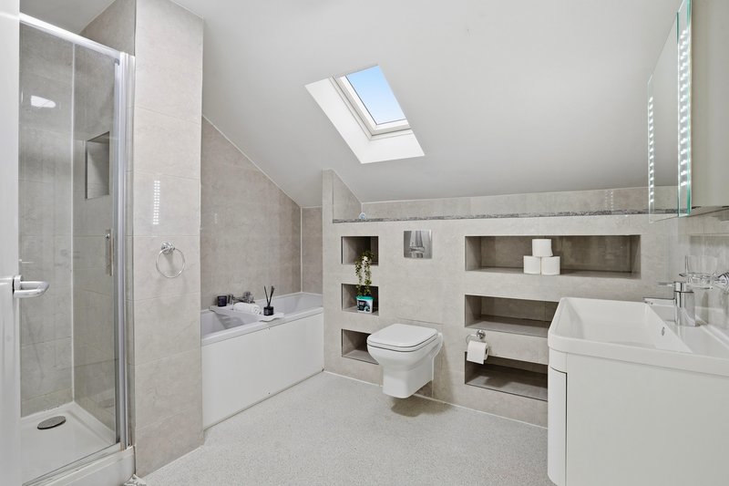Modern bathroom with shower enclosure, toilet, dual vanity sinks and skylight window