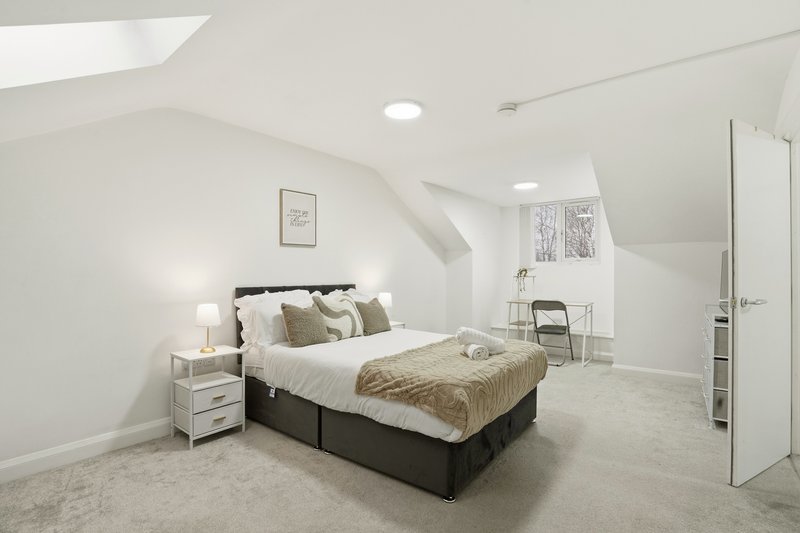 Bright attic bedroom with double bed, neutral bedding, white walls and carpeted floor.
