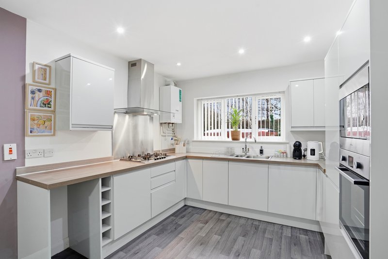 Modern white kitchen with wooden countertops, island, stainless steel appliances and vertical blinds