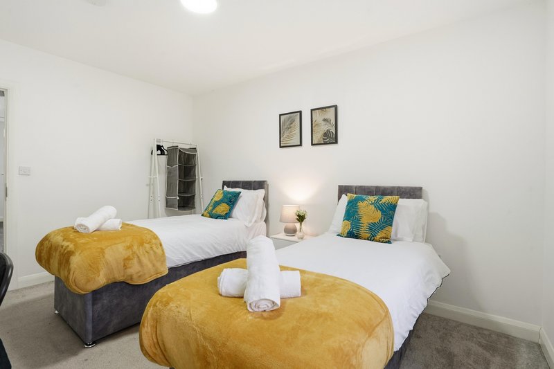 Twin bedroom with white bedding, gold poufs, green cushions and framed wall art