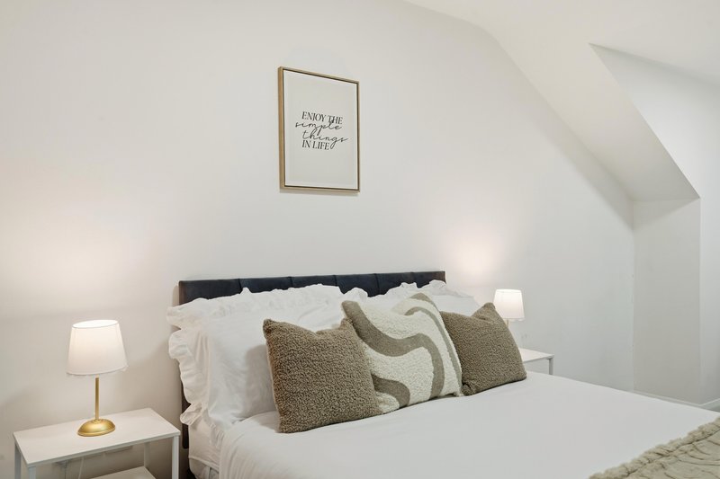 Bright bedroom with double bed, decorative pillows, bedside lamp, and framed wall art