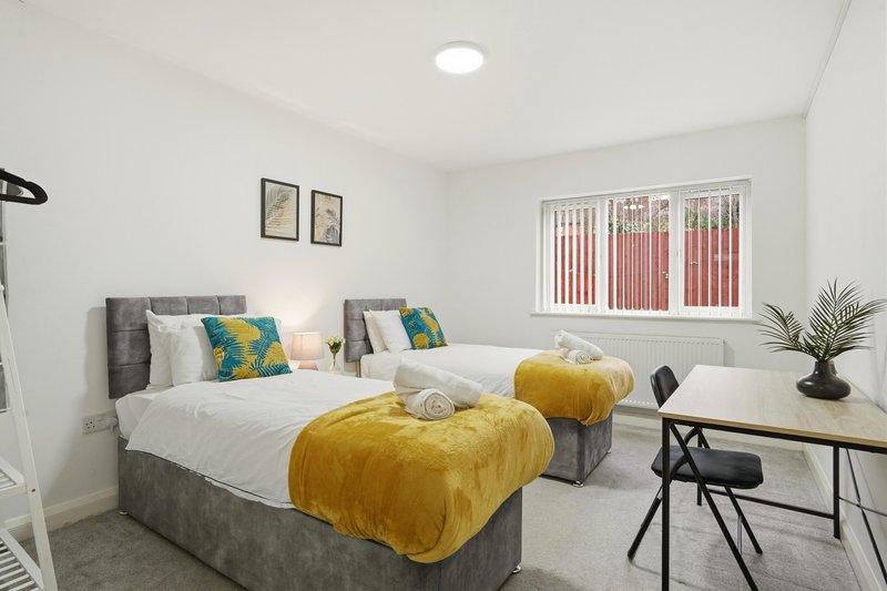 Bright bedroom with two single beds, yellow throws, desk, chair and potted plant