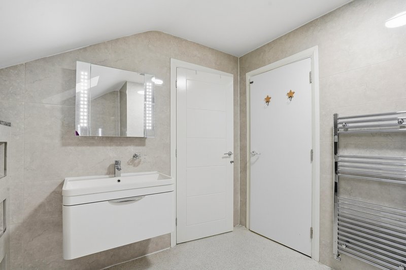Modern bathroom with white vanity, illuminated mirror, and heated towel rail