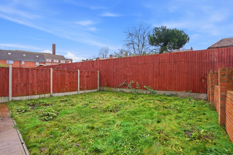 Outdoor garden space with red corrugated fencing, green lawn and brick outbuilding