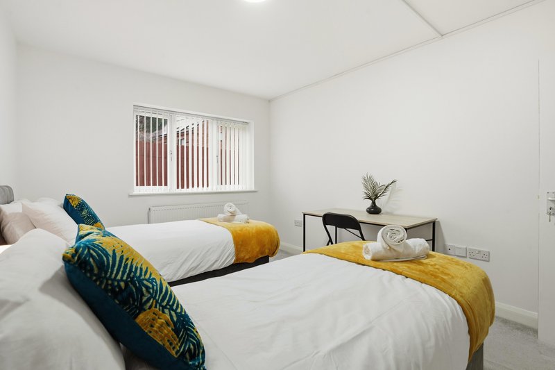 Bright twin bedroom with two single beds, colorful cushions, small desk and potted plant.