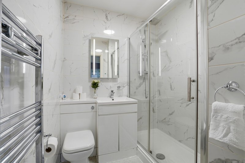 Modern bathroom with white marble tiles, double sink vanity, toilet, and glass shower enclosure