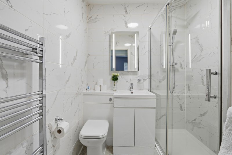 Modern bathroom with white marble tiles, vanity sink, toilet, and glass shower enclosure