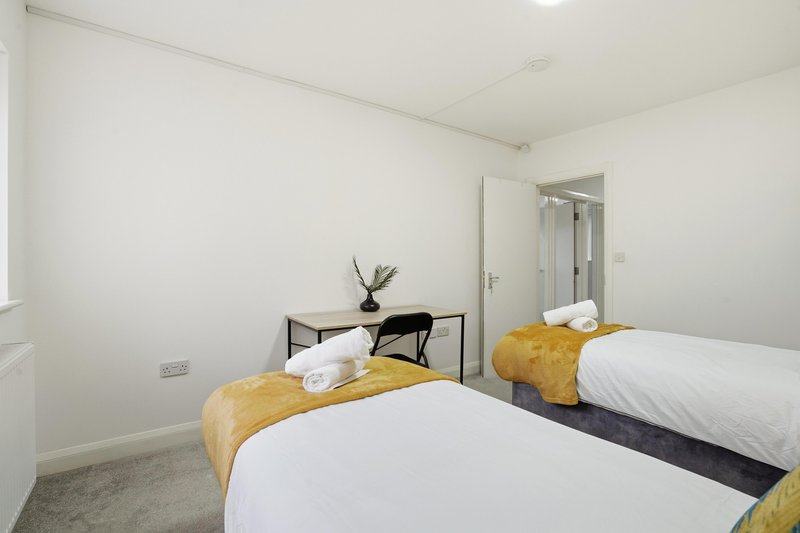 Modern bedroom with two single beds, white bedding, yellow cushions, and ensuite bathroom visible