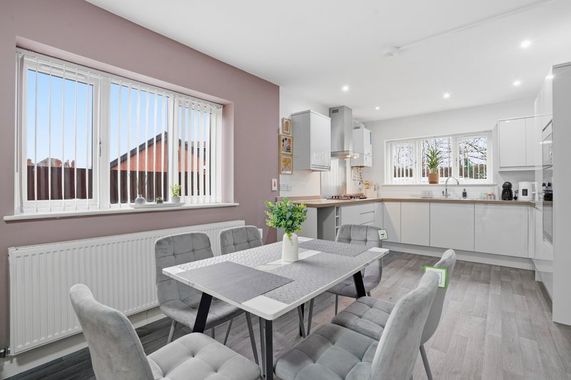 Modern open-plan kitchen and dining area with grey dining table, upholstered chairs, and white cabinetry
