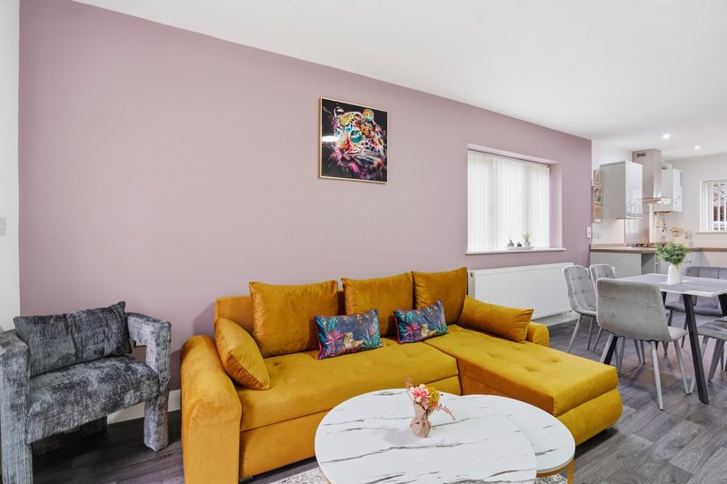 Living room with yellow corner sofa, pink walls, white marble table and dining area beyond