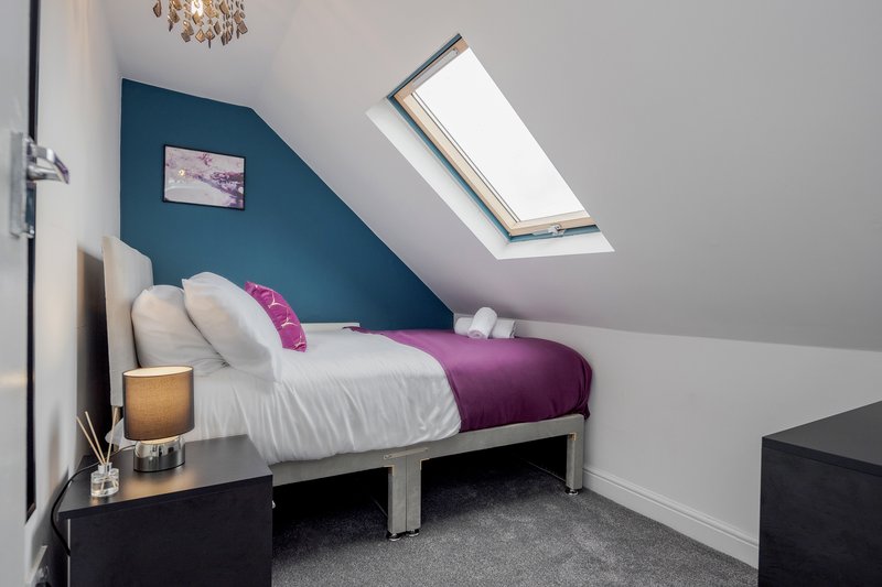 Attic bedroom with single bed, purple duvet, white pillows, skylight window and teal accent wall