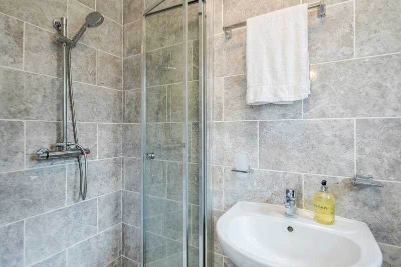 Modern bathroom with walk-in shower, white sink, and grey tile walls