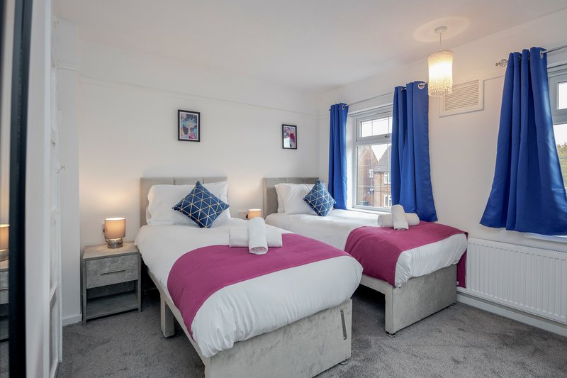 Bright bedroom with two single beds, pink and white bedding, blue curtains, wooden nightstands