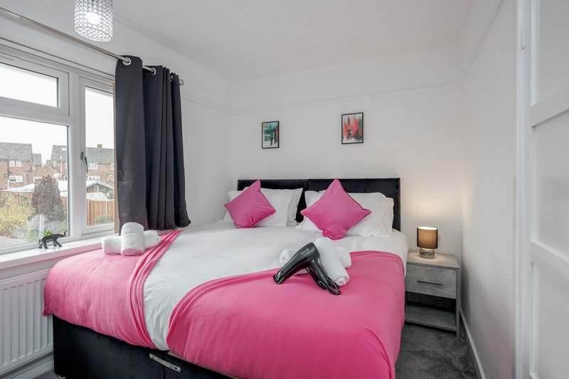 Bedroom with double bed, pink and white bedding, black headboard, window and bedside lamp