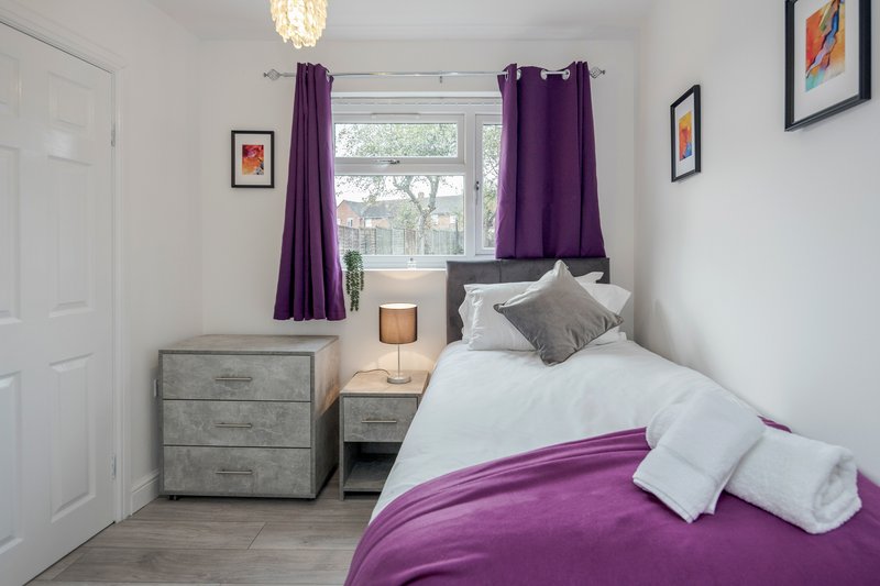 Bright bedroom with double bed, purple bedding and curtains, wooden floor, nightstand