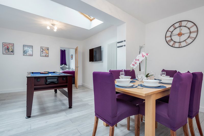 Open-plan living and dining area with purple chairs, wooden table, wall clock and skylights