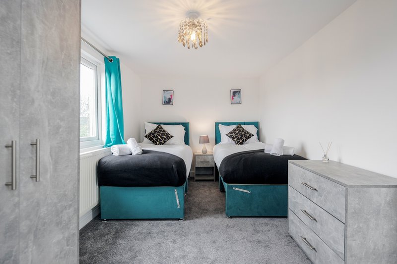 Twin bedroom with teal bed frames, white bedding, pendant light and window with curtains