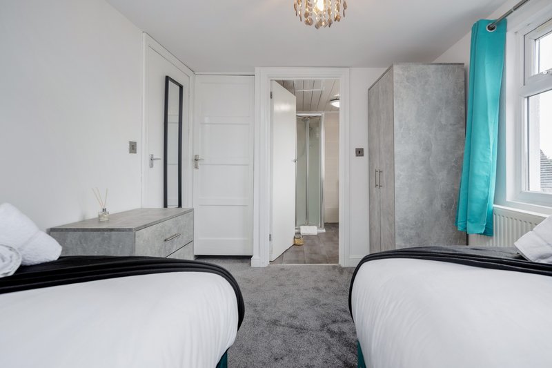 Bedroom with two single beds, gray carpet, white walls, and ensuite bathroom door