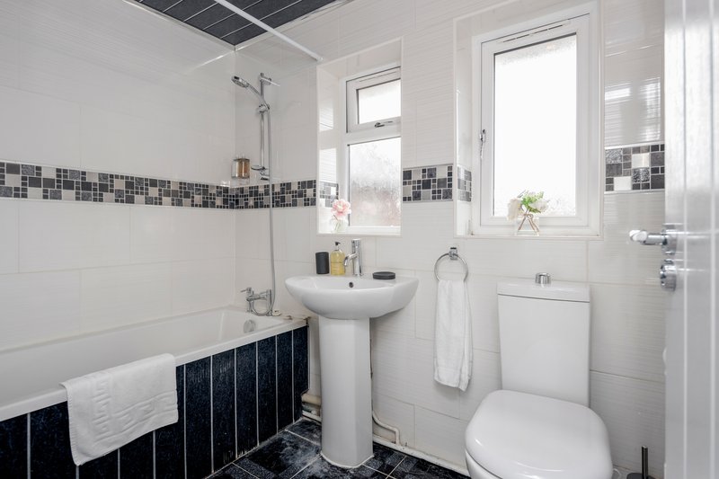 Bright bathroom with pedestal sink, toilet, bathtub and decorative tile border