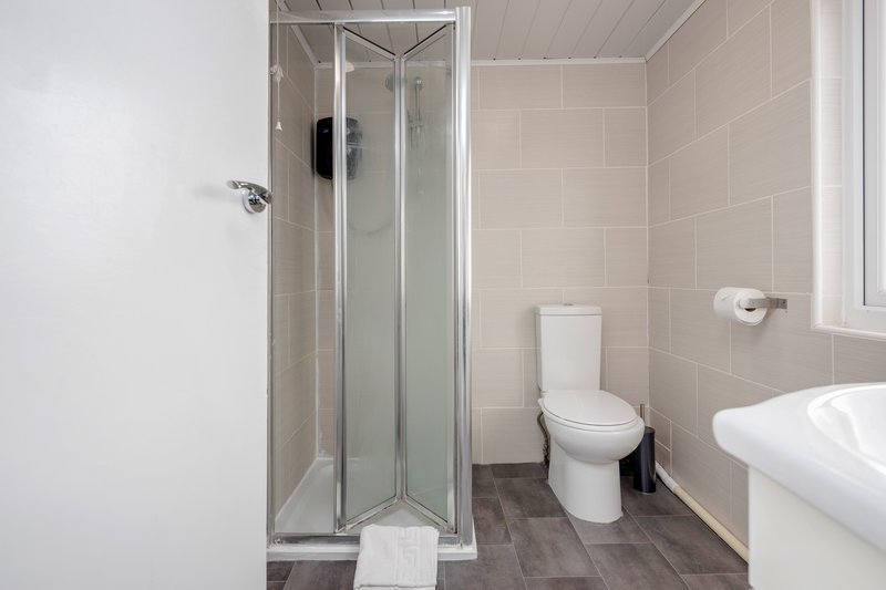 Clean modern bathroom with shower enclosure, toilet, sink and tiled walls