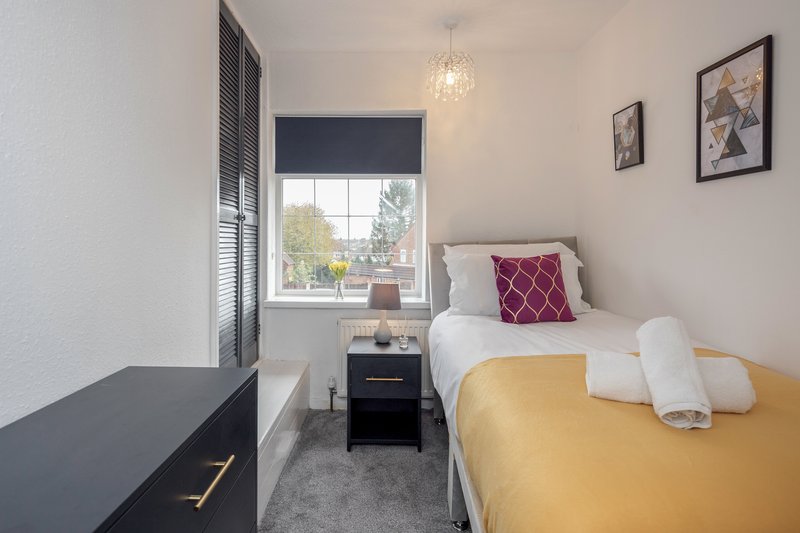 Bright bedroom with single bed, yellow bedding, black desk, window with garden view
