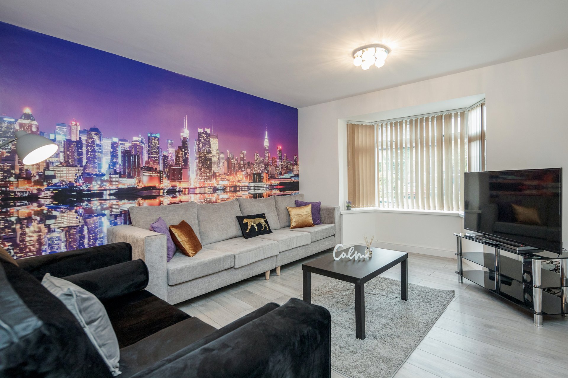 Modern living room with cityscape mural, light gray sofa, black armchair and TV unit