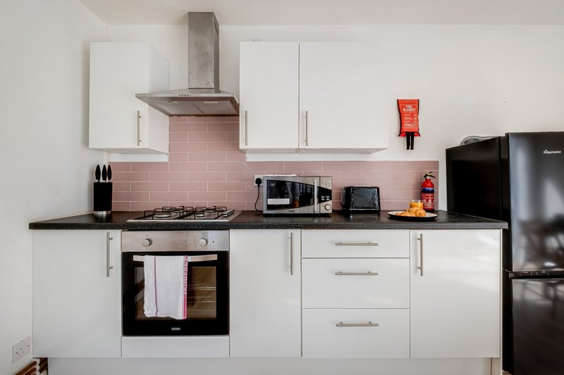 Modern kitchen with white cabinetry, pink tile backsplash, gas hob and stainless steel range hood