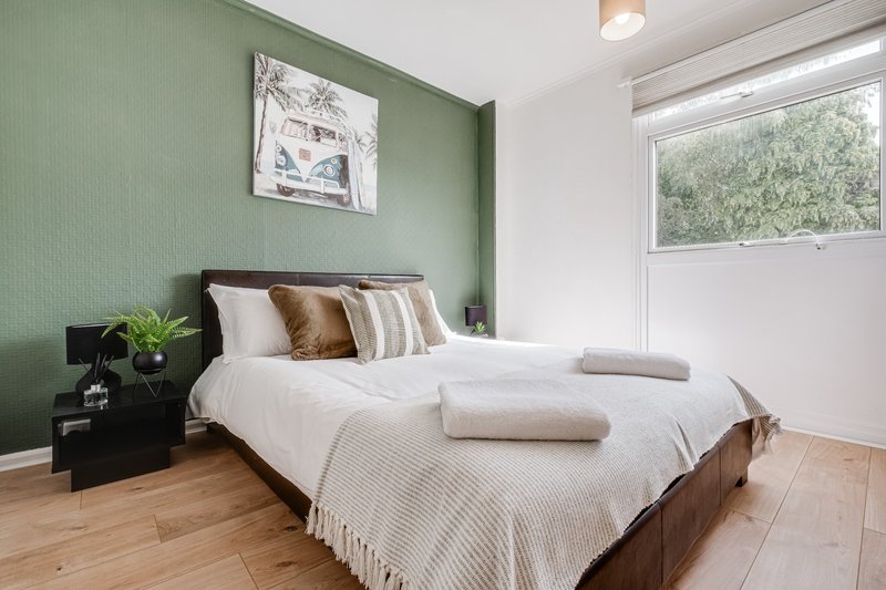 Bright bedroom with green walls, double bed, wooden floor and large window