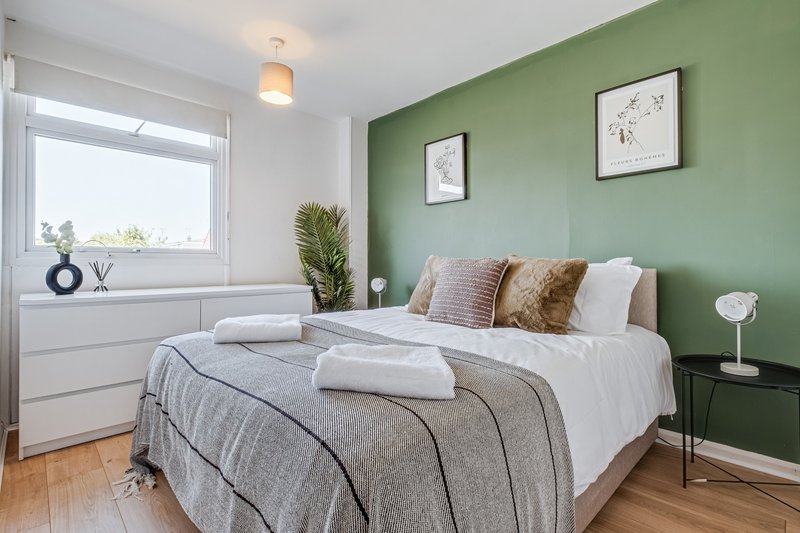 Bright bedroom with green accent wall, double bed, white bedding, wooden floor and window