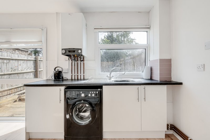 Modern utility room with white cabinetry, black countertop, integrated washing machine and window view