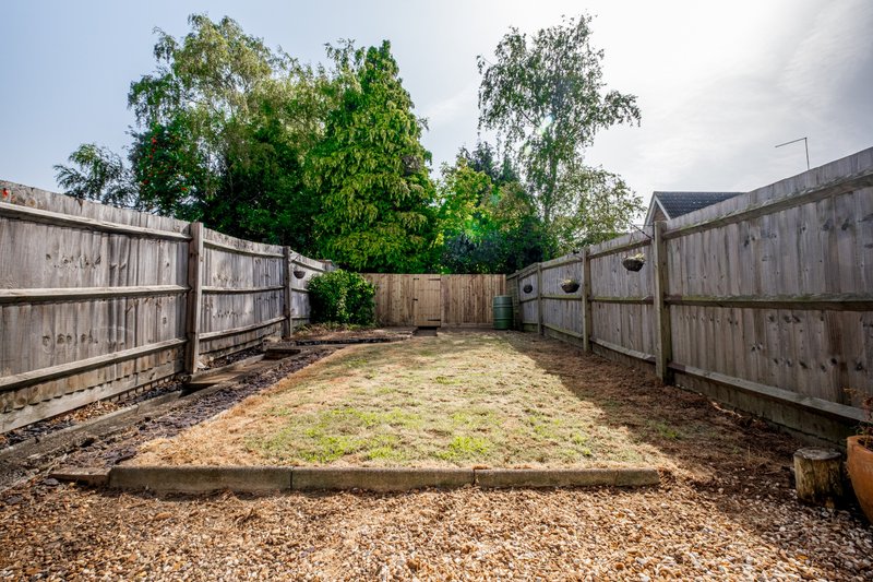 Fenced outdoor garden area with wooden gates, gravel surface, and mature trees