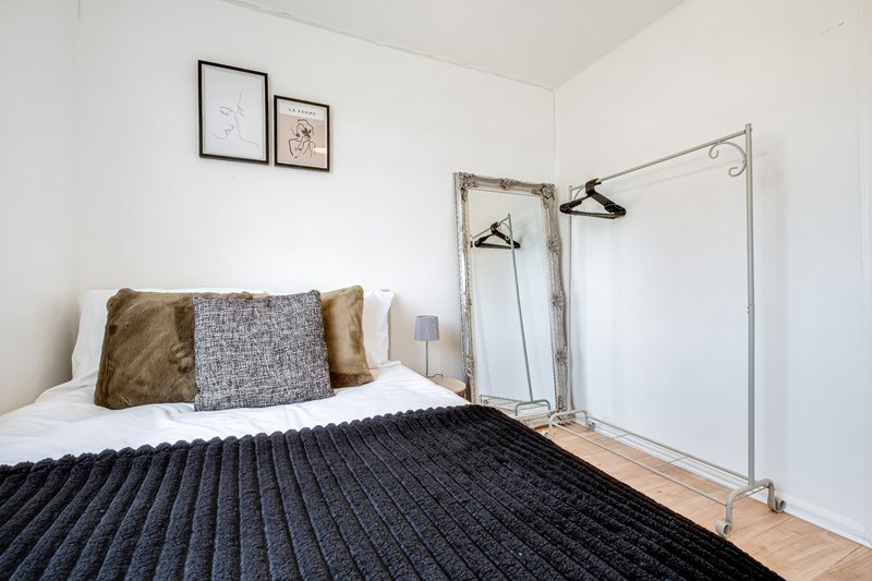 Bright bedroom with double bed, black ribbed bedding, gold and grey cushions, wooden flooring