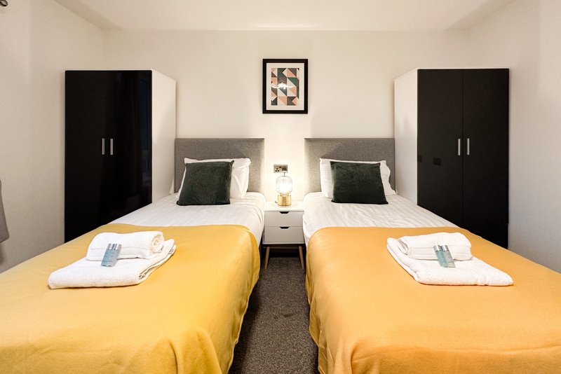 Modern twin bedroom with yellow bedding, black wardrobes, and framed wall art