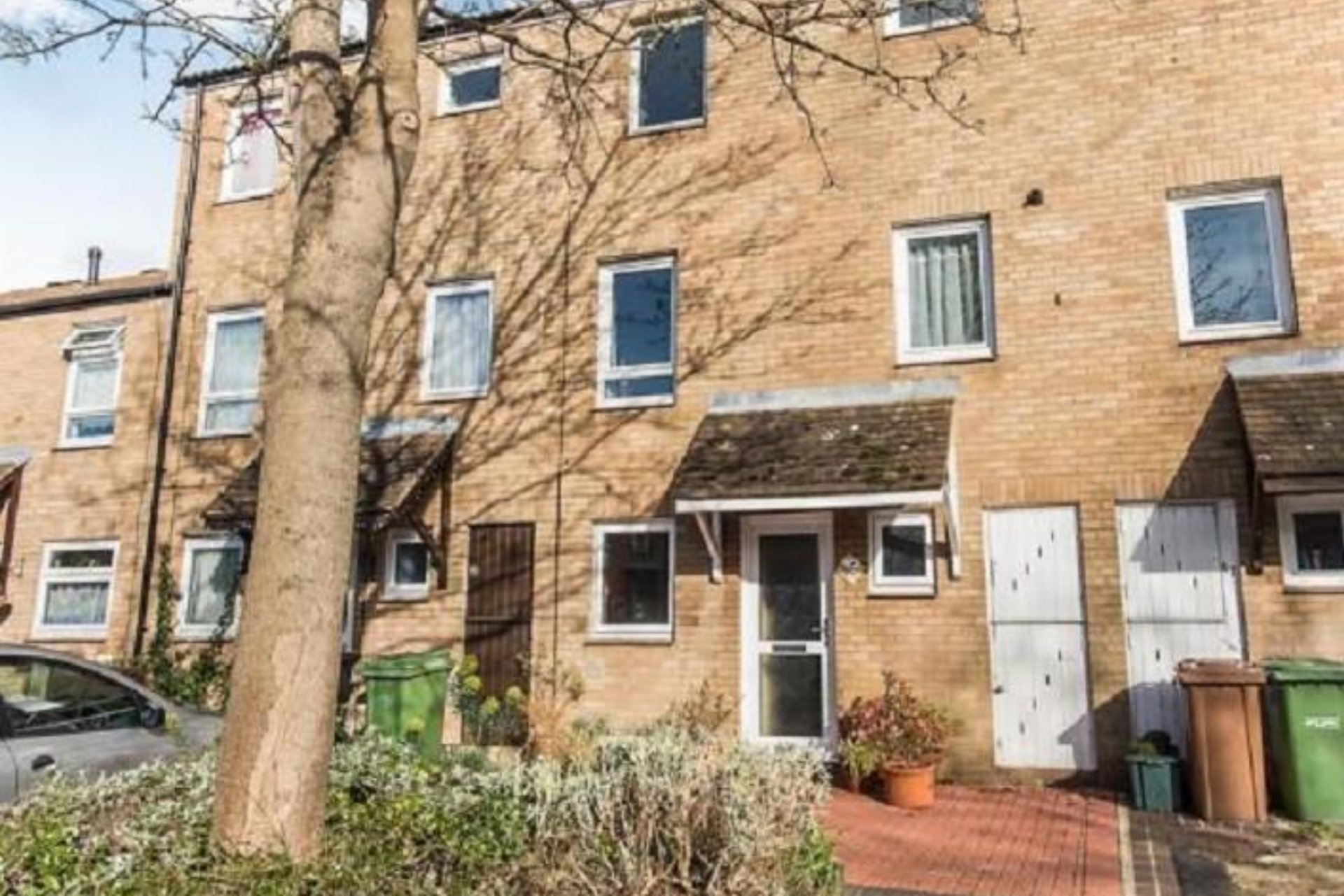 Brick terraced house with front door, windows, tree and brick patio area