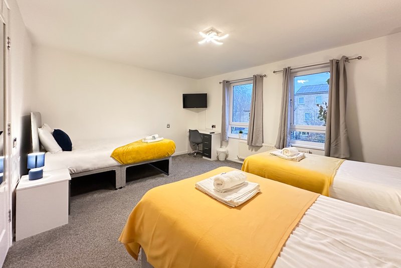 Bright twin bedroom with yellow bedding, wall-mounted TV, and windows overlooking street