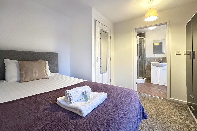 Bright bedroom with double bed, grey headboard, and en-suite bathroom visible through open door