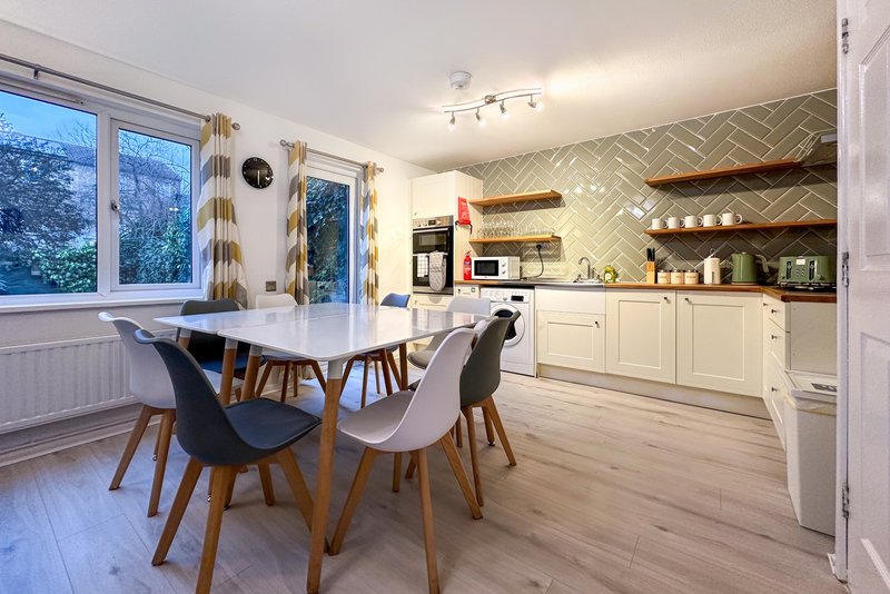 Modern kitchen and dining area with white cabinetry, dining table, chairs, and large windows