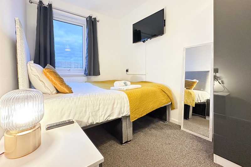 Bright bedroom with single bed, yellow bedding, wall-mounted TV and mirror