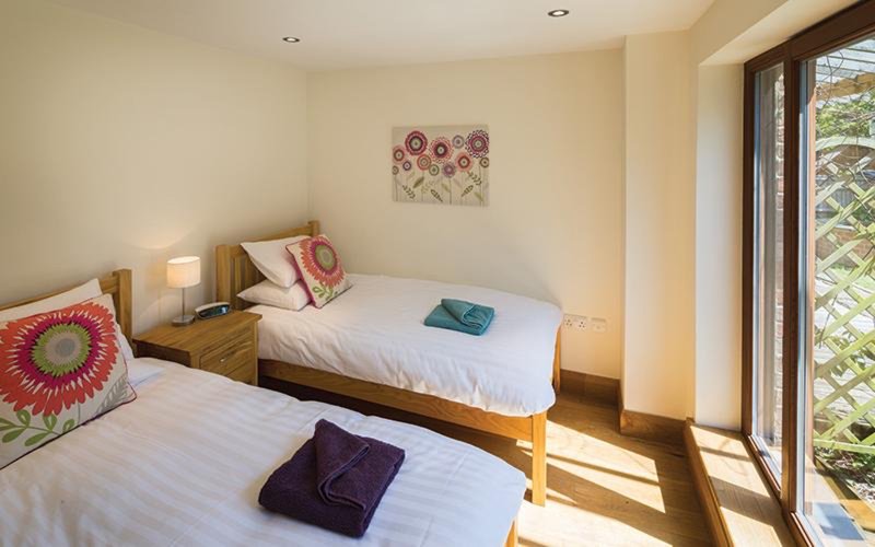 Bright bedroom with two single beds, wooden frames, colorful cushions and floral artwork