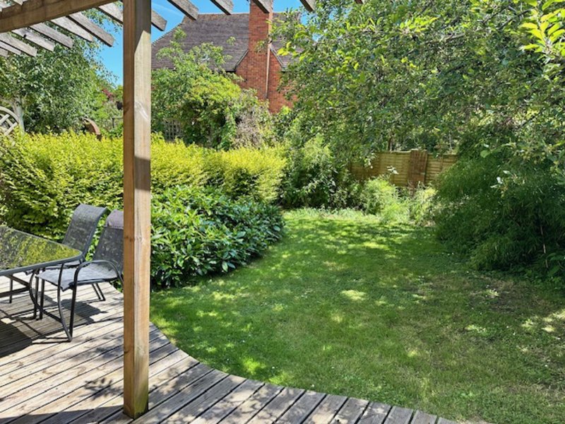 Garden view from wooden deck with pergola, lawn, hedges and brick building