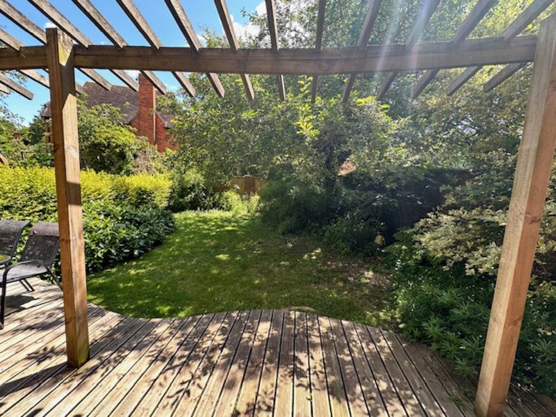 Wooden pergola and decking overlooking manicured garden with lawn and hedges
