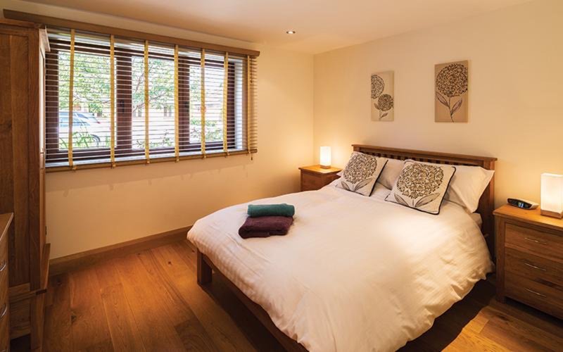 Warm bedroom with double bed, wooden furniture, shuttered windows and bedside lighting