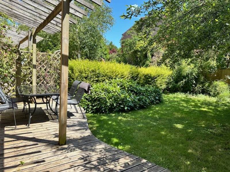 Garden with wooden deck, pergola, patio furniture and mature hedges and trees