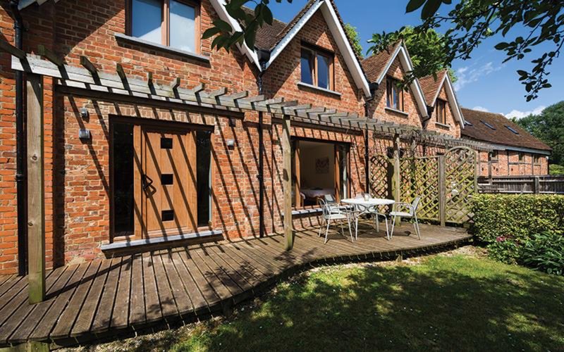Brick cottage exterior with wooden deck, garden seating area and green lawn