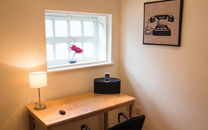 Desk workspace with lamp, window, speaker, and framed telephone artwork on wall