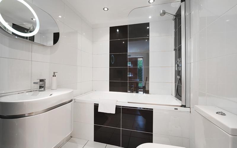 Modern bathroom with white tiles, curved sink, black cabinetry and glass shower enclosure