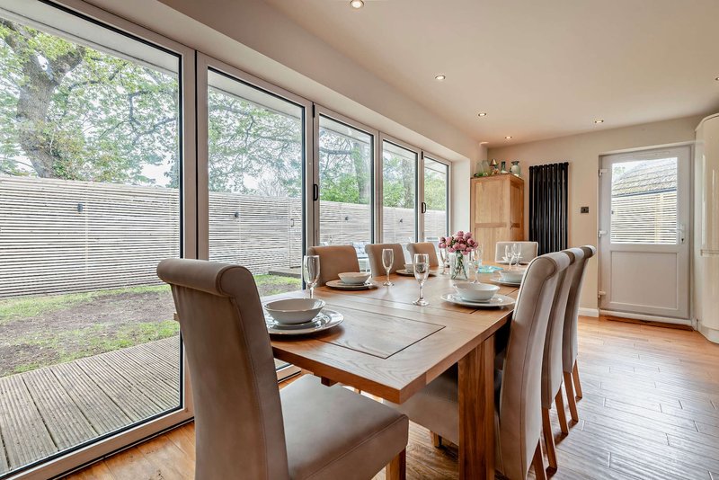 Modern dining room with wooden table, upholstered chairs, large garden doors and views